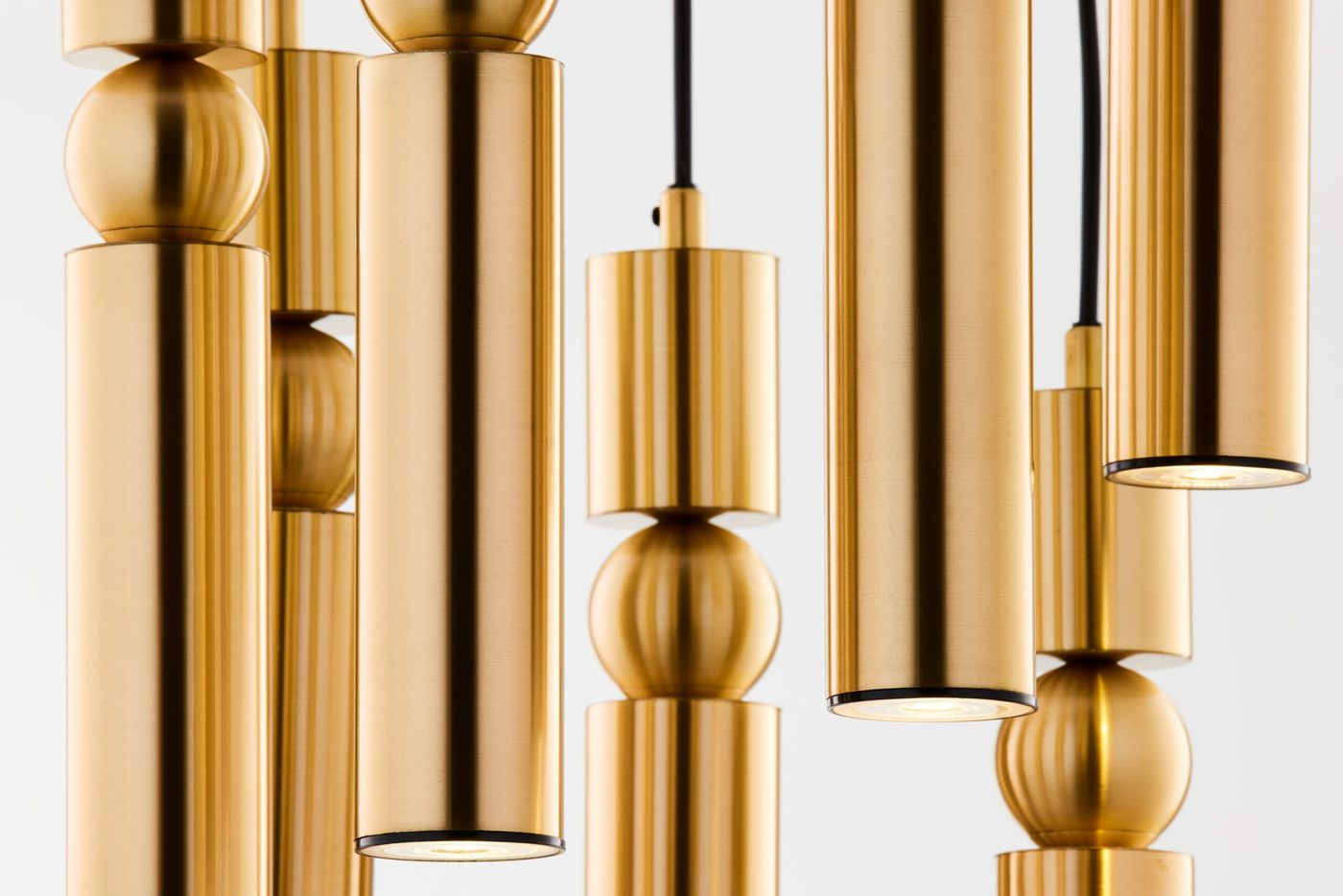 Lampa wisząca Alas w kolorze złotym, złożona z siedmiu cylindrycznych kloszy i kulistych elementów. Widoczna struktura materiału, z czarnym przewodem. Ujęcie z bliska, ukazujące detale i fakturę metalu.