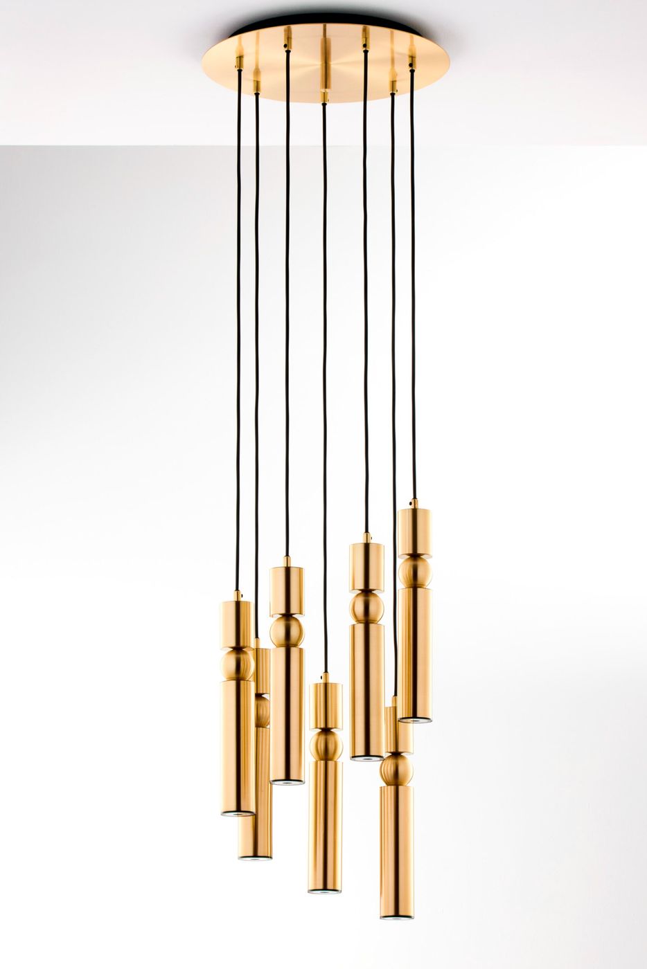 Lampa wisząca Alas w kolorze złotym z siedmioma oprawami na żarówki GU10. Zawieszona na czarnych kablach, z cylindrycznymi i kulistymi elementami. Kąt ujęcia frontalny, ukazujący elegancki design i nowoczesny styl.