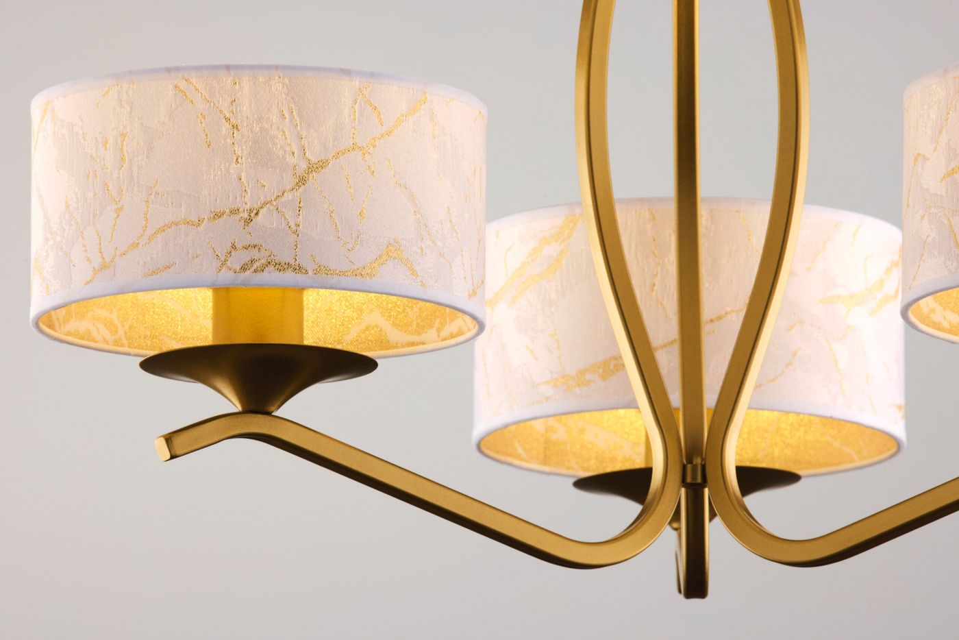 Kaszmir żyrandol w kolorze złotym z trzema kloszami E27 w białym odcieniu, zdobionymi złotymi wzorami. Ujęcie z boku, ukazujące detale kloszy i eleganckie, zaokrąglone ramiona. Idealny do stylowych wnętrz.