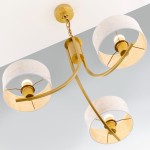 Żyrandol Arthur z trzema abażurami w kolorze białym z złotymi akcentami. Kształt okrągły, metalowa konstrukcja w złotym kolorze, z widocznymi źródłami światła E27. Ujęcie z dołu, z zawieszeniem na łańcuszku.