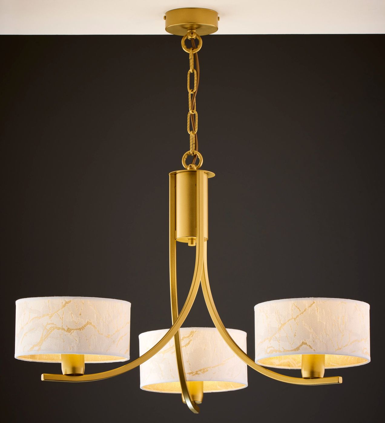 Żyrandol Arthur 3xE27 w kolorze złotym z białymi kloszami. Klosze mają delikatny wzór, a całość zawieszona na złotej łańcuchowej konstrukcji. Ujęcie z dołu, prezentujące szczegóły designu oraz wykończenia.