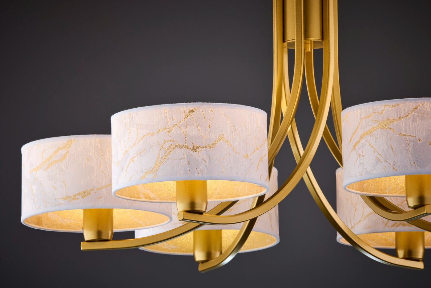 Żyrandol Arthur w kolorze złotym i białym, z sześcioma oprawami E27. Okrągłe klosze z białego materiału z delikatnym złotym wzorem, zawieszone na eleganckich, łukowatych ramionach. Widok z dołu, ukazujący szczegóły kloszy i konstrukcji.