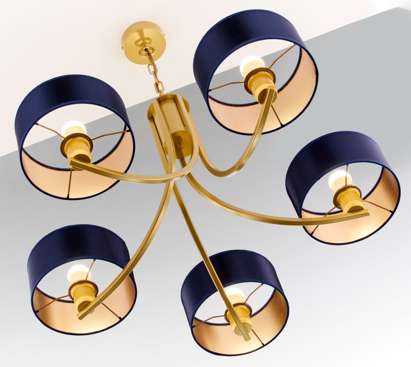 Żyrandol Arthur 5xE27 w kolorze złotym z granatowymi kloszami. Posiada pięć ramion z okrągłymi, materiałowymi kloszami, które mają złote wnętrze. Produkt montowany sufitowo, ukazany z dołu, w jasnym otoczeniu.