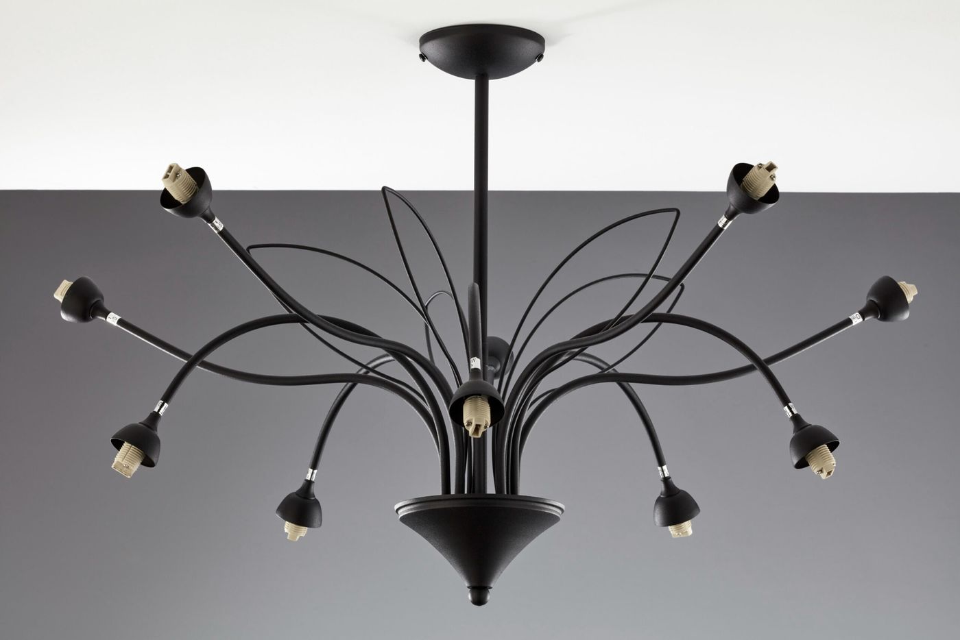 Żyrandol Gloriosa z 10 gniazdami G9 w kolorze czarnym i białym. Posiada elastyczne ramiona, które rozchodzą się promieniście z centralnej podstawy. Ujęcie z dołu, ukazujące szczegóły mocowania i kształt kloszy. Tło w odcieniach szarości.