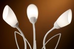 Lampa stołowa Gloriosa w kolorze piaskowo-szarym z trzema źródłami światła G9. Klosze w kształcie owalnym, wykonane z matowego szkła, zamocowane na białych, giętych ramionach. Ujęcie z bliska, ukazujące detale konstrukcji.