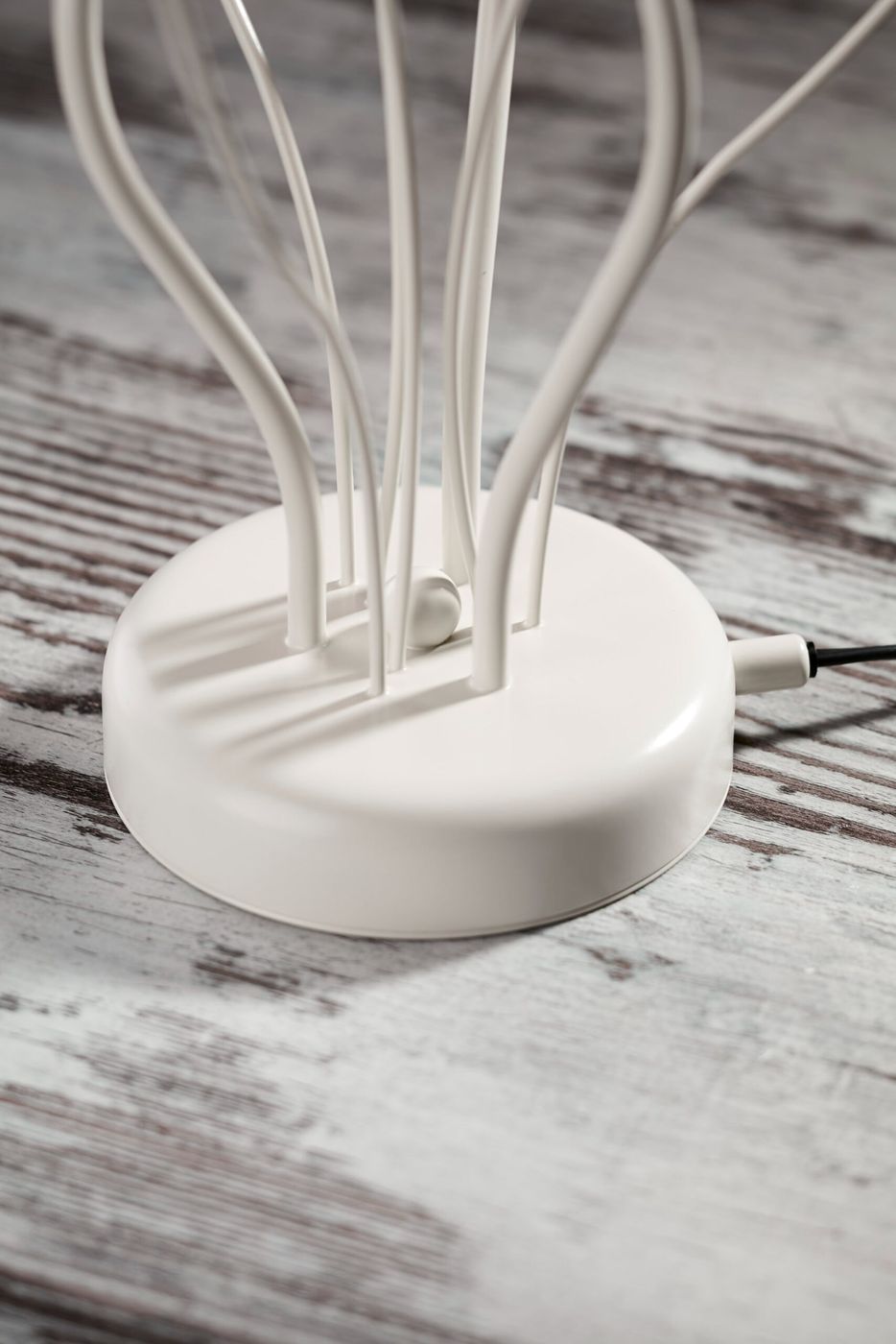 Lampa stołowa Gloriosa w kolorze piaskowo-szarym z białą podstawą. Widoczna okrągła baza z przewodami w stylu minimalistycznym. Ujęcie z boku, ukazujące detale konstrukcji i mocowania.