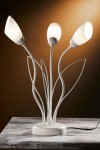 Lampa stołowa Gloriosa w kolorze piaskowo-szarym z trzema kloszami w kształcie tulipanów. Stojąca na okrągłej podstawie, z elastycznymi ramionami, które tworzą efekt roślinny. Widoczny kabel zasilający. Tło w ciepłym odcieniu.