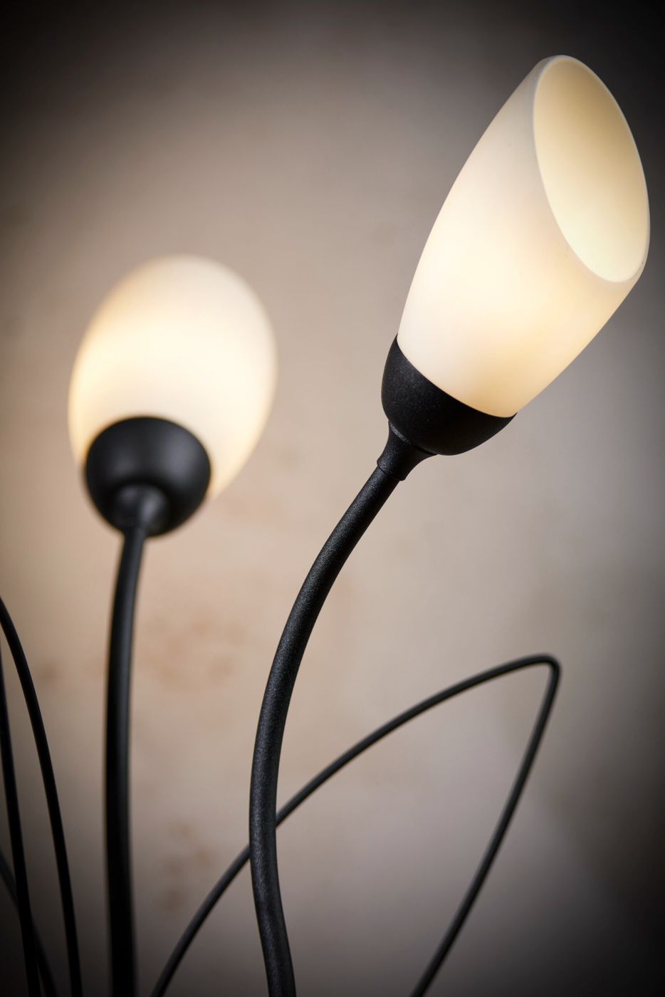 Lampa stołowa Gloriosa z trzema źródłami światła G9, z czarnym metalowym stelażem i białymi kloszami w kształcie kielicha. Produkt przedstawiony w zbliżeniu, z widocznymi, delikatnie wygiętymi ramionami. Tło w odcieniach szarości.