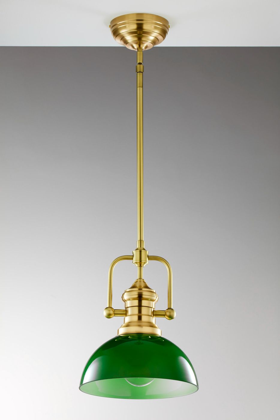 Lampa wisząca Platino 1xE27 w mosiądzu szczotkowanym z zielonym kloszem. Produkt zawieszony na długim, mosiężnym stelażu, z dekoracyjnymi detalami i wykończeniem w stylu retro. Tło w odcieniach szarości.