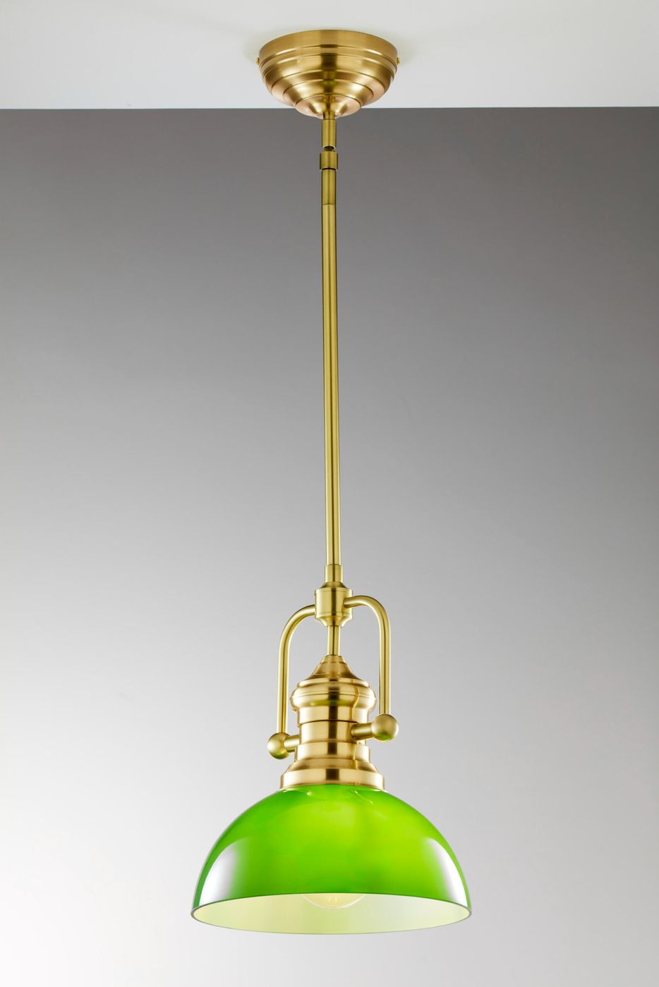 Lampa wisząca Platino z mosiądzu szczotkowanego w kolorze zielonym. Posiada okrągły klosz w intensywnym odcieniu zieleni, zawieszona na długim, złotym ramieniu. Klosz ma gładką, błyszczącą powierzchnię. Ujęcie frontalne, na jednolitym tle.