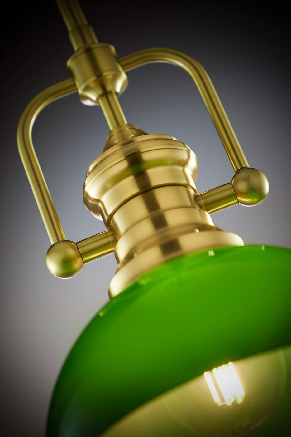 Lampa wisząca Platino z mosiądzu szczotkowanego w kolorze zielonym, z okrągłym kloszem i detalem w postaci metalowego uchwytu. Produkt widoczny z bliska, ukazuje detale mocowania oraz struktury materiału. Idealna do nowoczesnych wnętrz.