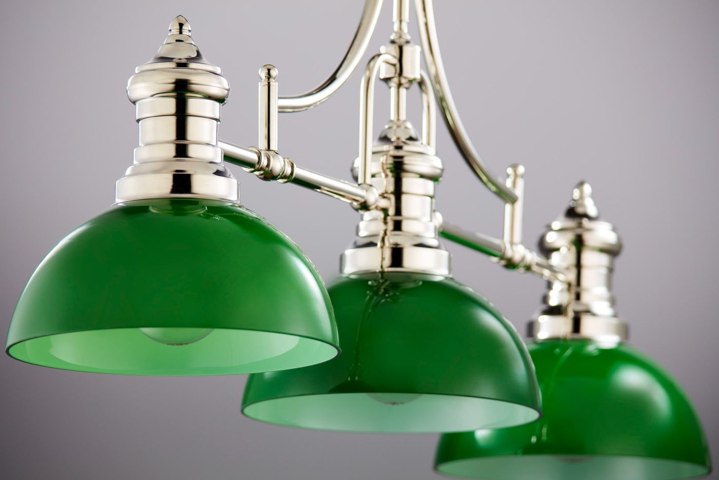 Lampa wisząca Platino 3xE27 w kolorze zielonym z niklowanym wykończeniem. Posiada trzy szklane klosze o zaokrąglonym kształcie, zawieszone na metalowej konstrukcji z eleganckimi detalami. Ujęcie z przodu, ukazujące detal i wykończenie.