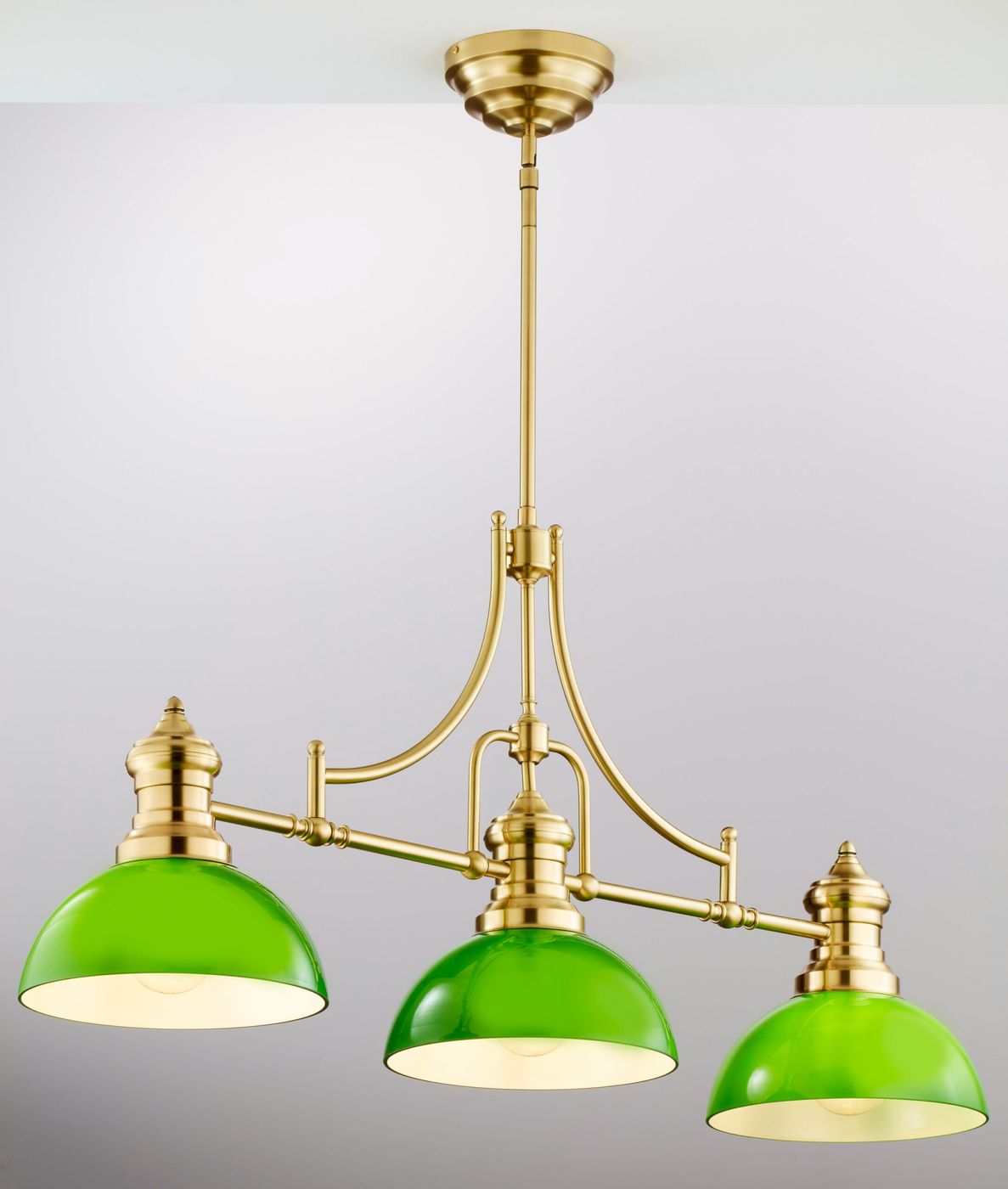 Lampa wisząca Platino z mosiądzu szczotkowanego w kolorze zielonym, z trzema kloszami o kształcie półkuli. Produkt zawieszony na prostym, eleganckim ramieniu. Klosze wykonane z przezroczystego szkła, zapewniające ciepłe światło.