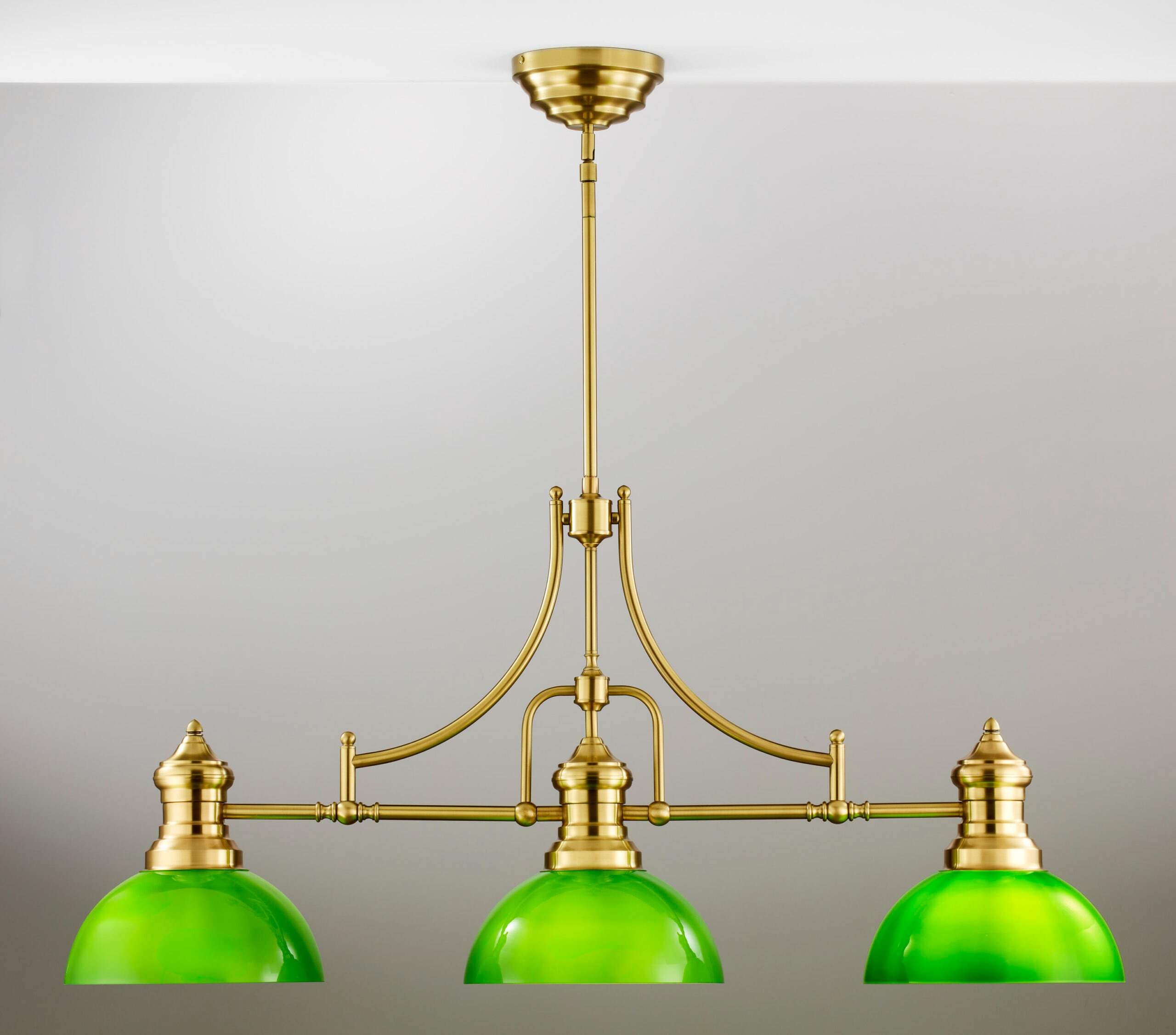 Lampa wisząca Platino z trzema kloszami w kolorze zielonym, wykonana z mosiądzu szczotkowanego. Ujęcie frontalne, z zawieszeniem na długim pręcie. Klosze mają zaokrąglony kształt, a elementy konstrukcyjne są widoczne. Tło jasne i jednolite.