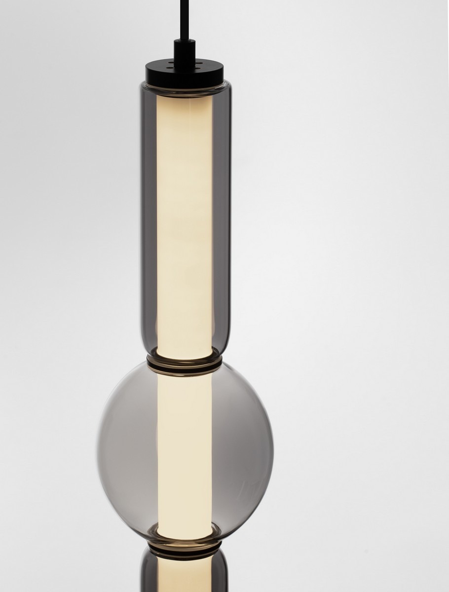 Lampa wisząca Glorica 1xLED 15W w kolorze czarnym, z cylindrycznym kloszem i kulistą bazą z przezroczystego szkła. W centralnej części umieszczony źródło światła LED, zawieszona na cienkim przewodzie. Tło jasne, minimalistyczne.