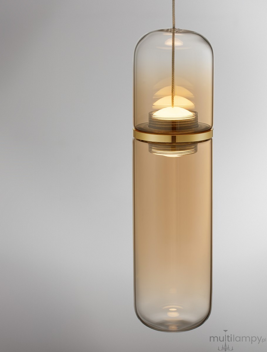 Lampa wisząca Rebalvo 1xLED 7W w złotym kolorze. Szklany klosz w kształcie cylindrycznym, z przezroczystą powierzchnią, zawieszony na cienkim sznurku. Widoczna źródło światła w górnej części. Tło jasne, minimalistyczne.