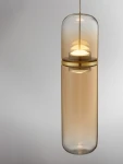 Lampa wisząca Rebalvo 1xLED 7W w złotym kolorze. Szklany klosz w kształcie cylindrycznym, z przezroczystą powierzchnią, zawieszony na cienkim sznurku. Widoczna źródło światła w górnej części. Tło jasne, minimalistyczne.