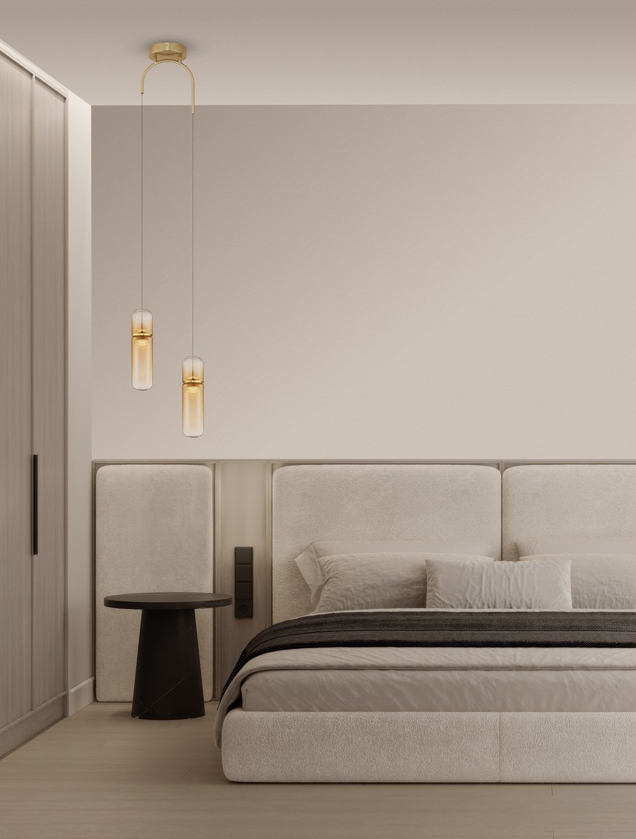 Lampa wisząca Rebalvo 2xLED 14W w kolorze złotym, z dwiema szklanymi kloszami w kształcie cylindrów, zawieszona na cienkich linkach. Produkt umieszczony w nowoczesnej sypialni z jasnymi ścianami i minimalistycznym wystrojem.