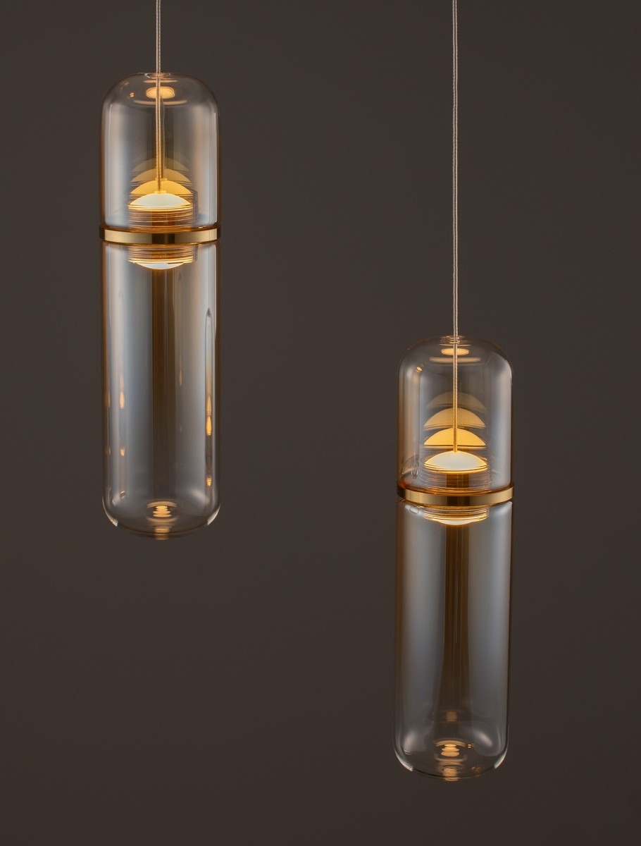 Lampa wisząca Rebalvo z dwoma źródłami światła LED 14W, w złotej oprawie. Szklane klosze w kształcie cylindrów, zawieszone na cienkich linkach, emitujące ciepłe światło. Tło ciemnoszare, podkreślające elegancki design lampy.