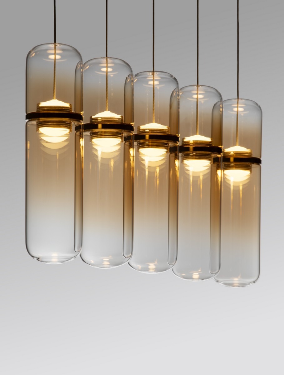 Lampa wisząca Rebalvo z pięcioma żarówkami LED o mocy 35W, w złotym wykończeniu. Szklane klosze w kształcie cylindrów, zawieszone na cienkich linkach, emitują ciepłe światło, nadając elegancki wygląd. Ujęcie z przodu.