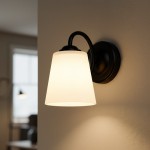 Kinkiet Pafos 1xE27 w kolorze czarnym. Lampa z matowym kloszem w kształcie stożka, zamontowana na okrągłej podstawie. Ujęcie z boku, pokazujące detal mocowania oraz emitowane światło na ścianie.