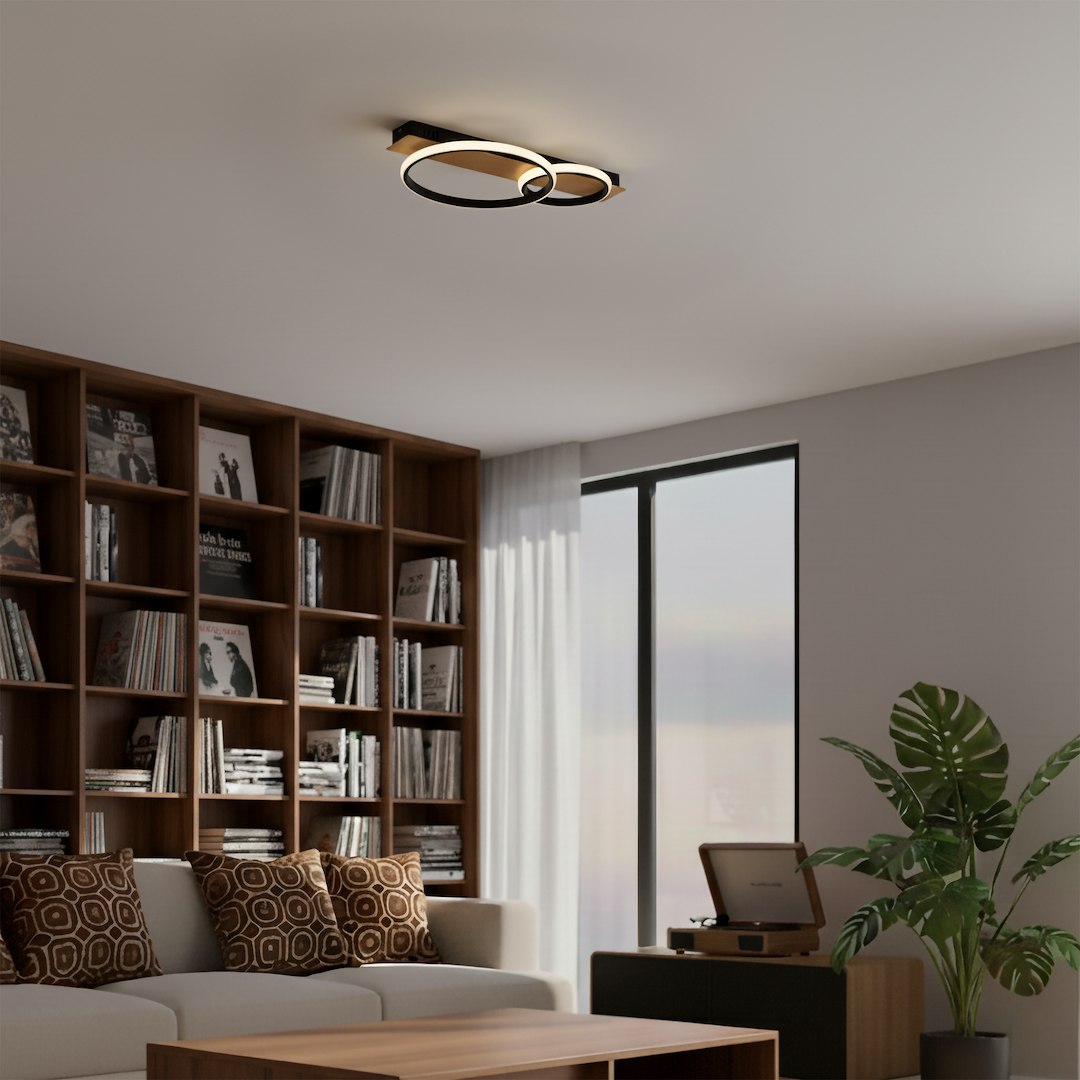 Czarna lampa sufitowa LED Rowena 14W 4000K z dwoma okrągłymi pierścieniami, zamontowana na suficie. Oświetlenie nowoczesne, w minimalistycznym stylu, idealne do wnętrz. Tło z regałem książek i rośliną w doniczce.