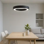 Lampa wisząca LED Union 40W CCT w czarnym kolorze, okrągła, zawieszona nad drewnianym stołem. W tle biały ściana z rośliną w wazonie i szarym sofą. Idealna do nowoczesnych wnętrz.