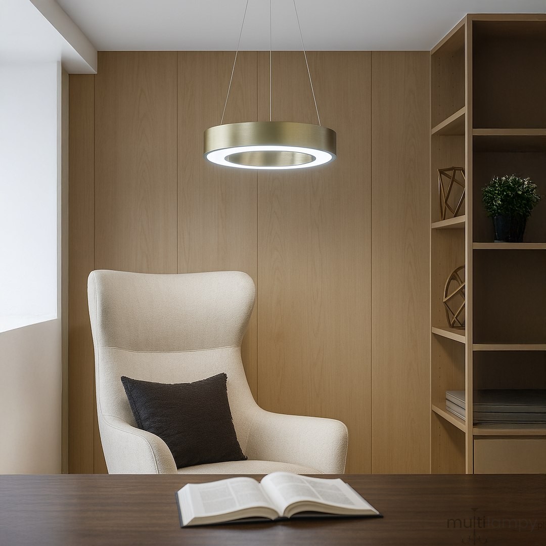 Lampa wisząca LED Union 40W CCT w kolorze złotym, okrągła, zawieszona nad jasnym fotelem. W tle drewniana ściana i regał z dekoracjami. Oświetlenie emitujące białe światło, wykończenie metaliczne.