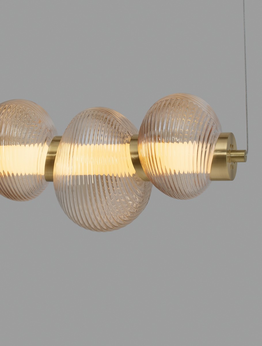 Lampa wisząca Tanvera z jedną żarówką LED 30W, złota z bursztynowymi, żłobionymi kloszami. Ujęcie z przodu, pokazujące trzy okrągłe klosze na metalowej podstawie, zawieszone na cienkim przewodzie. Tło szare, minimalistyczne.