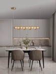 Lampa wisząca Tanvera 1xLED 30W w kolorze złotym z bursztynowymi kloszami, zawieszona nad stołem w nowoczesnej jadalni. Widoczne eleganckie krzesła oraz dekoracyjne elementy, takie jak kwiaty w wazonie i świeczki na stole.