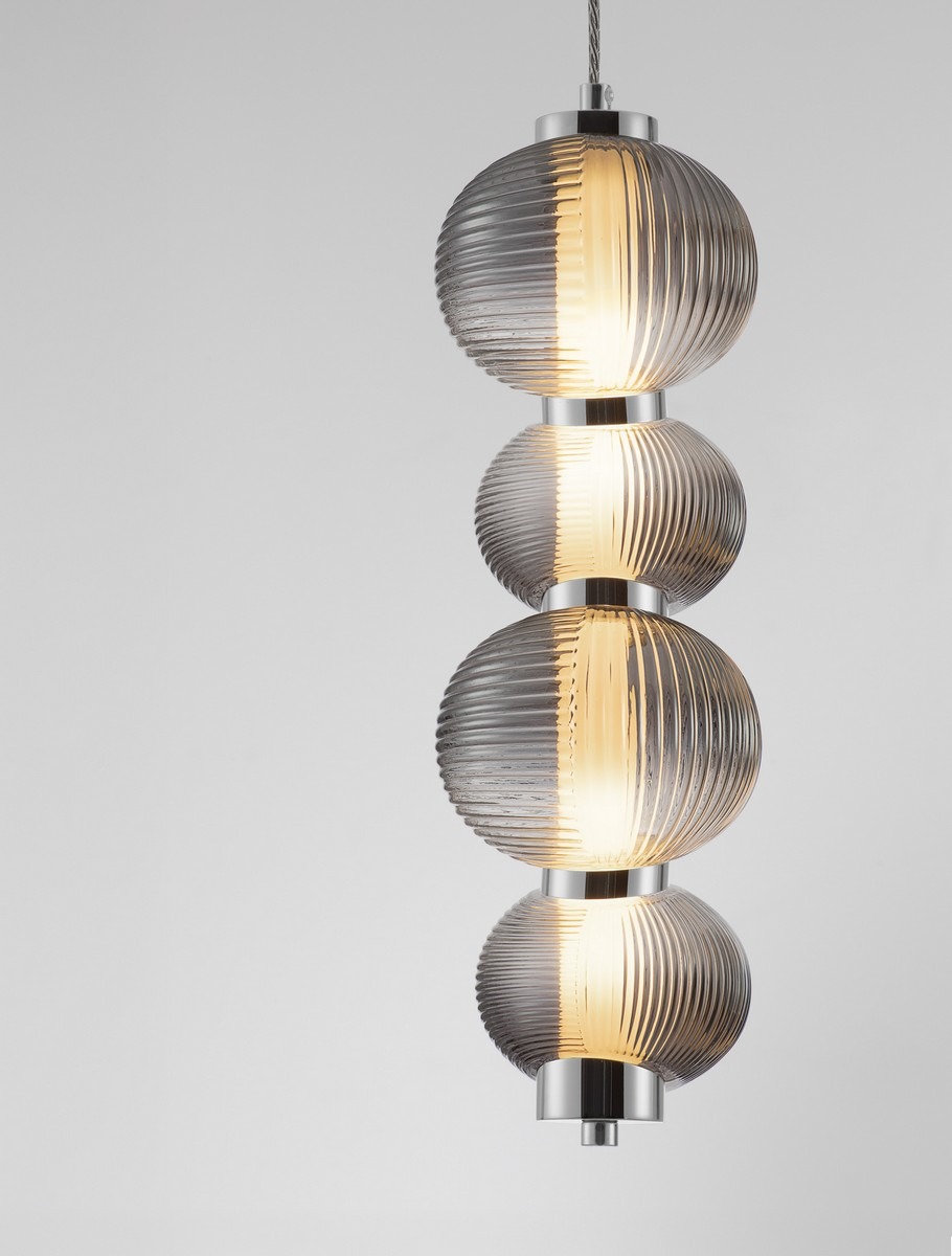 Lampa wisząca Tanvera z trzema okrągłymi kloszami z przezroczystego szkła w odcieniu szarym, z wyraźnymi żłobieniami. Metalowe detale w kolorze chromu. Ujęcie frontalne, wisząca konstrukcja, źródło światła LED 15W. Tło jednolite, jasne.