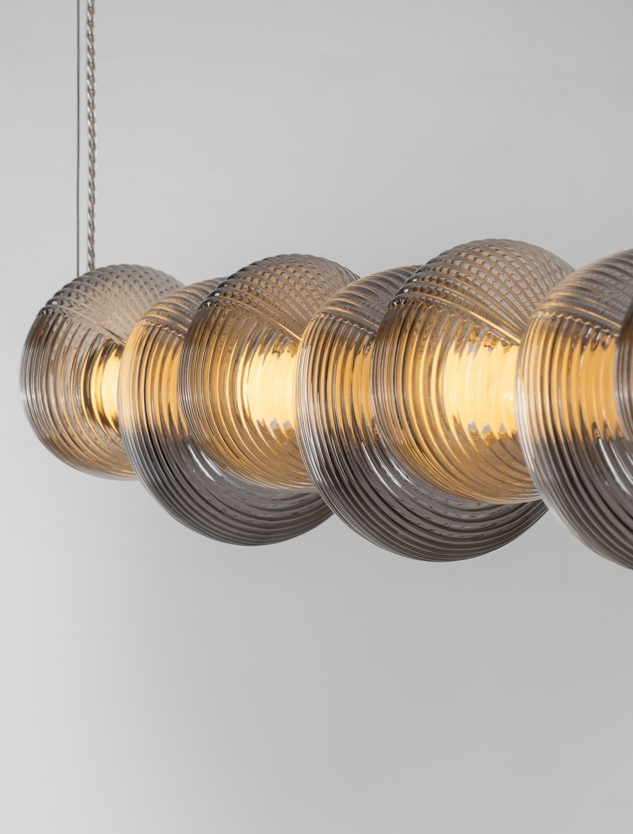 Lampa wisząca Tanvera z jednym źródłem LED 30W w chromowanym wykończeniu. Składa się z sześciu okrągłych kloszy w szarym, teksturowanym szkle, zawieszonych na metalowym przewodzie, z ciepłym światłem wewnątrz.
