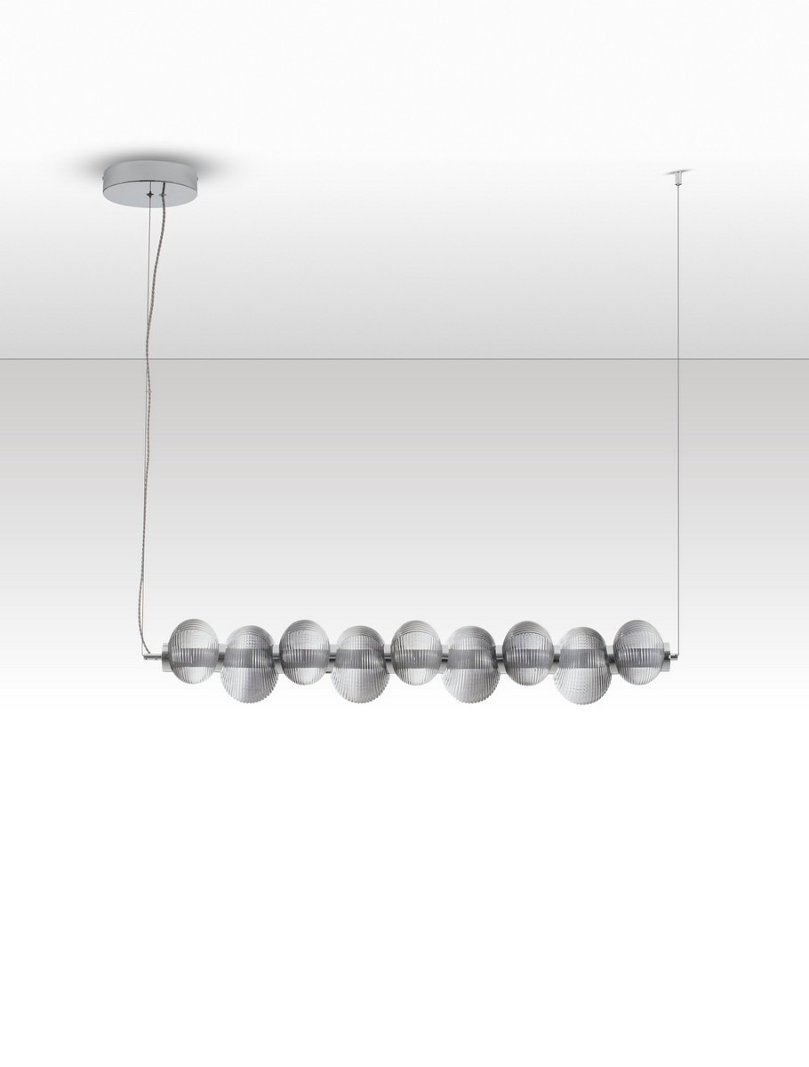 Lampa wisząca Tanvera z jednym źródłem LED 30W, w kolorze chromu i szarości. Posiada osiem szklanych, cylindrycznych kloszy z wyraźnym żłobieniem, zawieszona na cienkim kablu. Montowana do sufitu na okrągłej podstawie.