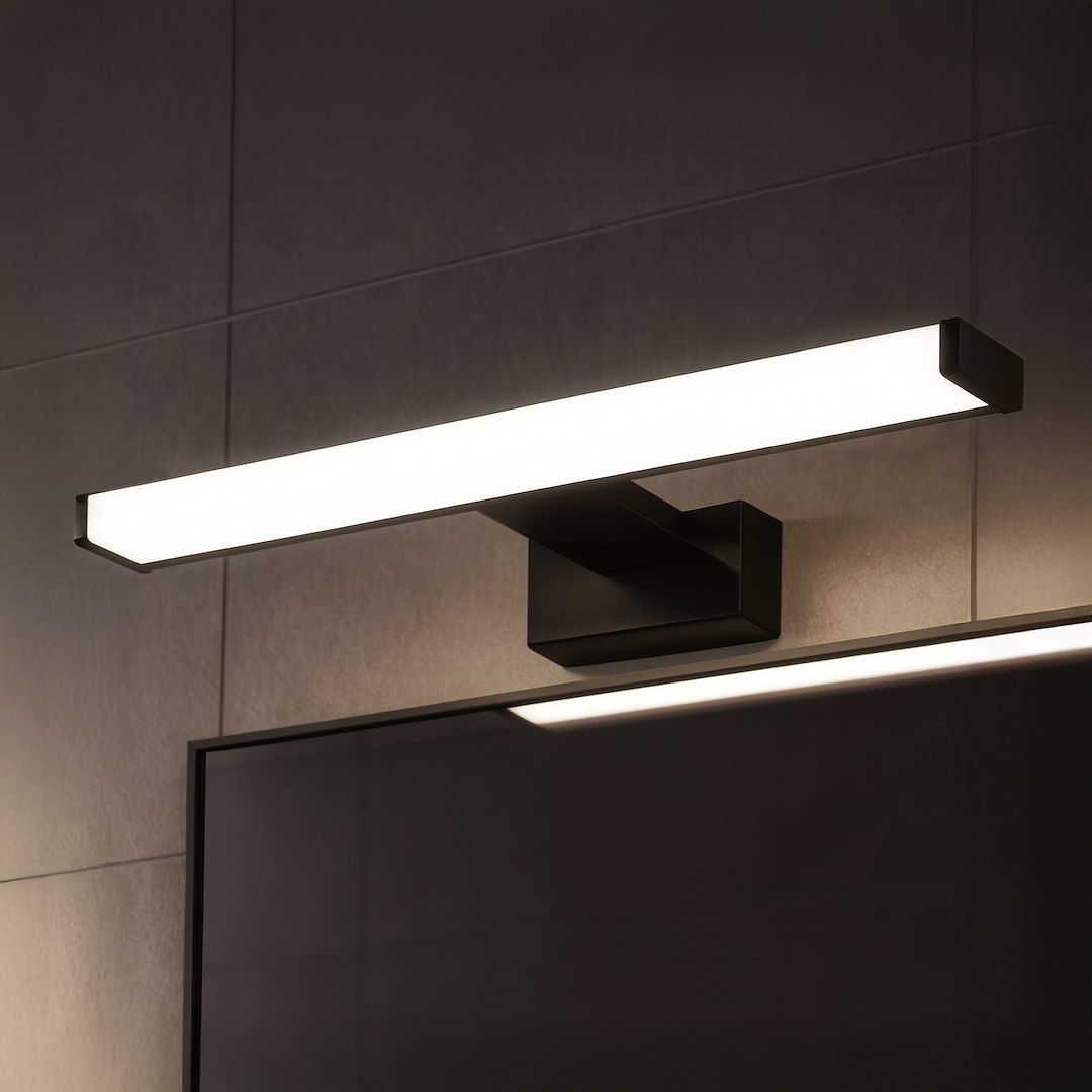 Kinkiet Mirore L40 LED 8W 4000K w kolorze czarnym, montowany na ścianie, o prostokątnym kształcie. Emituje białe, równomierne światło. Widoczny montaż do lustra na tle szarej ściany. Wodoszczelność IP44.