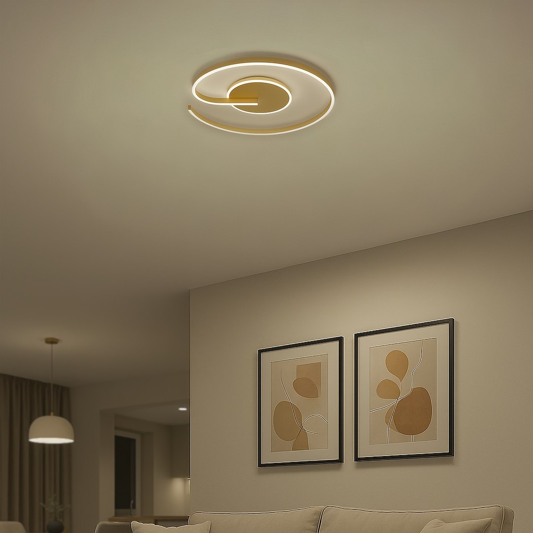 Lampa sufitowa LED Lorenzo 22W 4000K w kolorze złotym, o nowoczesnym, spiralnym kształcie, zamontowana na suficie. W tle widoczne abstrakcyjne obrazy w ramkach oraz jasna sofa, tworzące elegancką aranżację wnętrza.