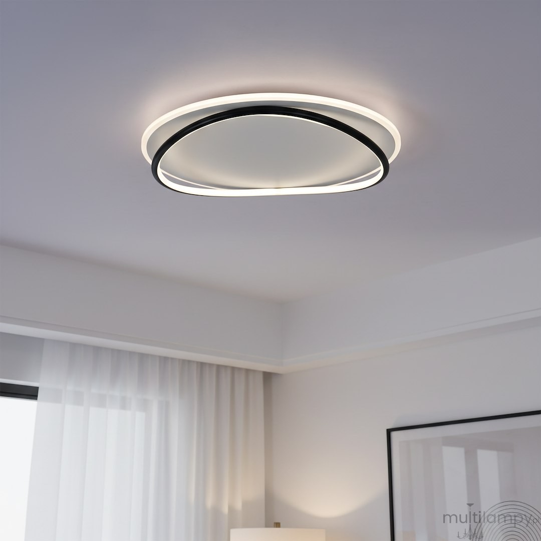 Lampa sufitowa LED Halo 38W z białym kloszem i czarną ramą, o okrągłym kształcie. Zawieszona na suficie, emituje neutralne światło 4000K. Widoczna w nowoczesnym wnętrzu z zasłonami i lampą stojącą.
