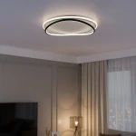 Lampa sufitowa LED Halo 38W w kolorze czarnym i białym, okrągła, z matowym kloszem i podświetleniem. Zawieszona na suficie w nowoczesnym wnętrzu, obok okna z zasłonami, w lekko oświetlonym pomieszczeniu.