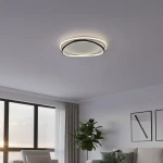 Lampa sufitowa LED Halo 38W, 4000K, w kolorze czarno-białym, o okrągłym kształcie. Zainstalowana na suficie, emituje jasne, neutralne światło. Tło to nowoczesne wnętrze z oknem, rośliną i sofą.
