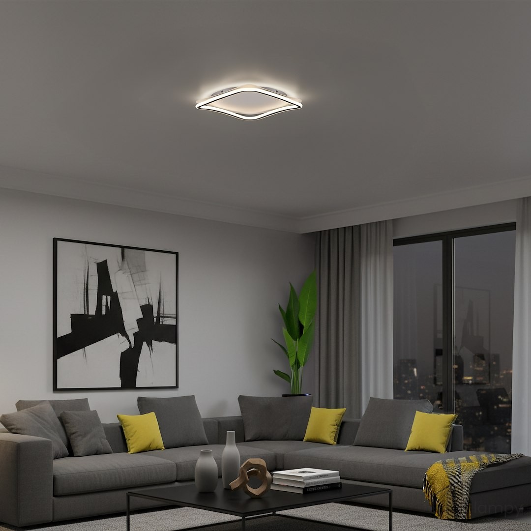 Cali Square lampa sufitowa LED 30W 4000K w kolorze czarnym i białym, zamontowana na suficie. Posiada nowoczesny, falisty kształt. W tle widoczny salon z szaro-żółtą sofą, obrazem oraz rośliną.