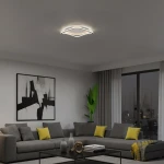 Cali Square lampa sufitowa LED 30W 4000K w kolorze czarnym i białym, zamontowana na suficie. Posiada nowoczesny, falisty kształt. W tle widoczny salon z szaro-żółtą sofą, obrazem oraz rośliną.