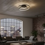 Lampa sufitowa LED Turner 32W 4000K w czarnym kolorze, złożona z dwóch spiralnych pierścieni, zamontowana na suficie. Widoczna w nowoczesnym wnętrzu z kanapą i dużym oknem. Tło z cegły i rośliny dodają charakteru aranżacji.