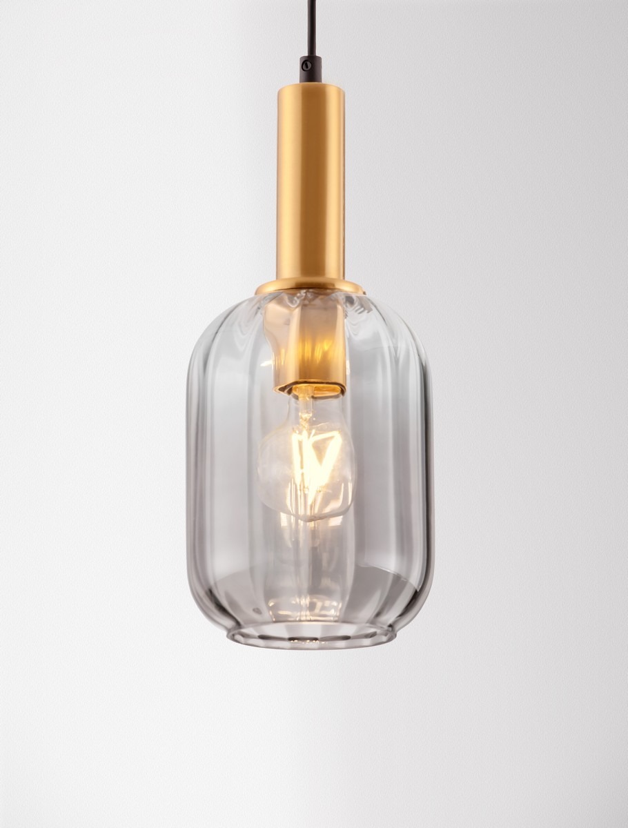 Lampa wisząca Querisa z przezroczystego szkła, z metalowym złotym uchwytem. Kształt cylindryczny z widoczną żarówką E27 w środku. Powieszone na czarnym przewodzie, idealna do nowoczesnych wnętrz. Tło białe.