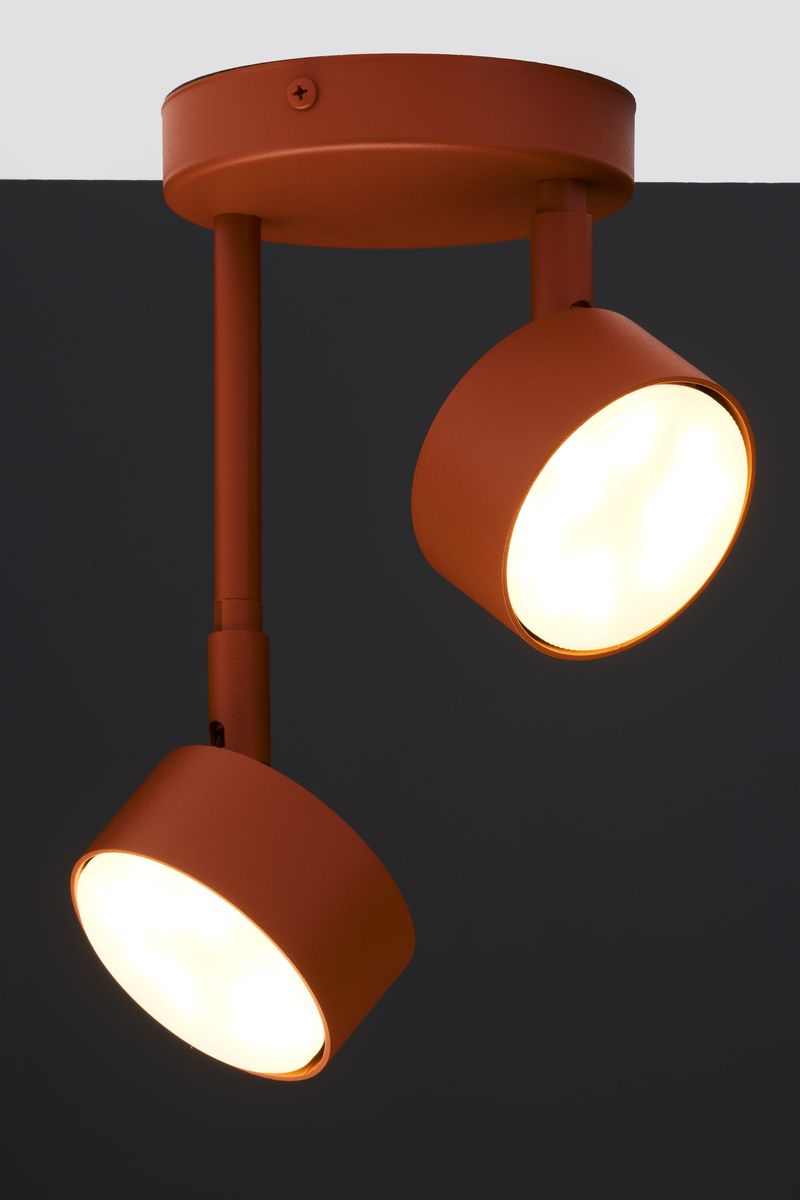 Lampa wisząca Nemo 2xGX53 w kolorze ceglastym z dwoma okrągłymi kloszami. Klosze są zamocowane na metalowych prętach, emitując ciepłe światło. Ujęcie z boku, na jednolitym ciemnym tle, ukazuje detale konstrukcji i fakturę materiału.