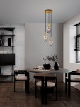 Lampa wisząca Querisa z trzema żarówkami E27 w złotym wykończeniu, zawieszona na czarnych linkach, z przezroczystymi kloszami. Umieszczona nad okrągłym stołem w nowoczesnym wnętrzu z drewnianą podłogą i minimalistycznym tłem.