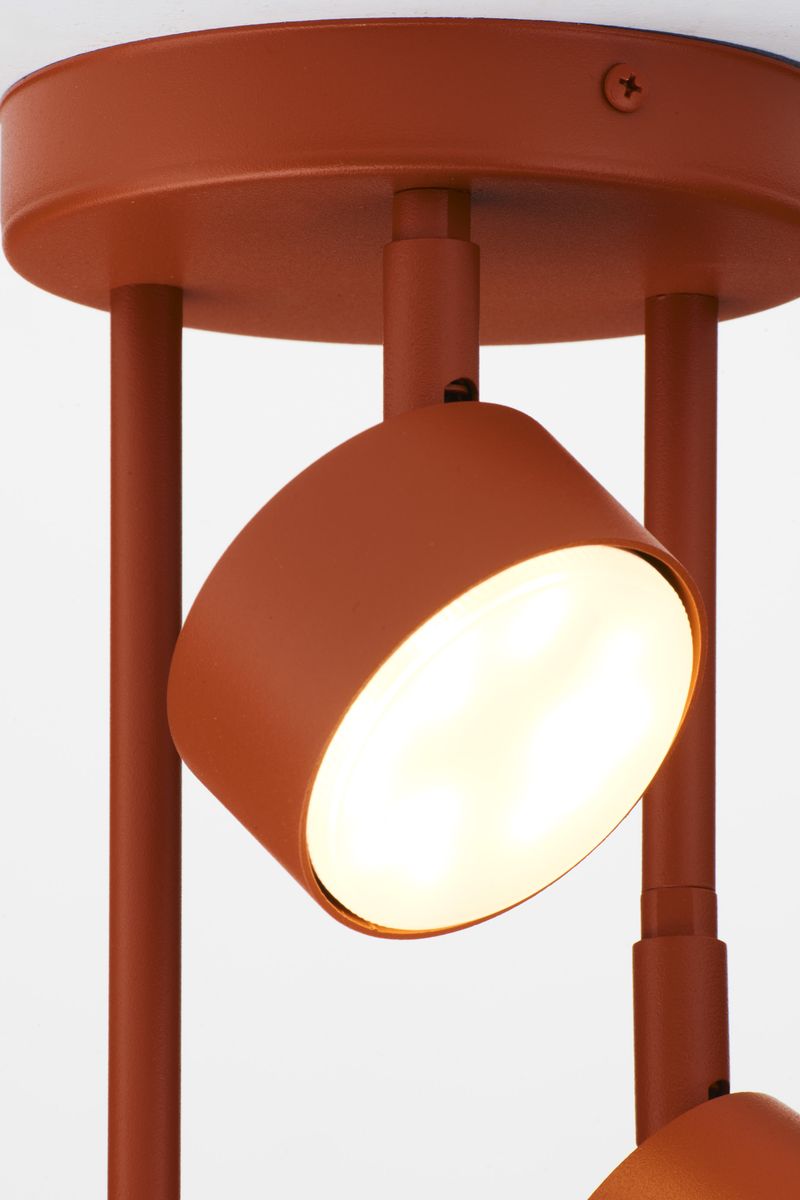 Lampa wisząca Nemo w kolorze ceglastym z trzema punktami świetlnymi na okrągłej podstawie. Ujęcie z bliska, ukazujące jeden z kloszy, wykonany z matowego metalu, emitujący ciepłe światło. Elementy montażowe w kolorze dopasowanym do kloszy.