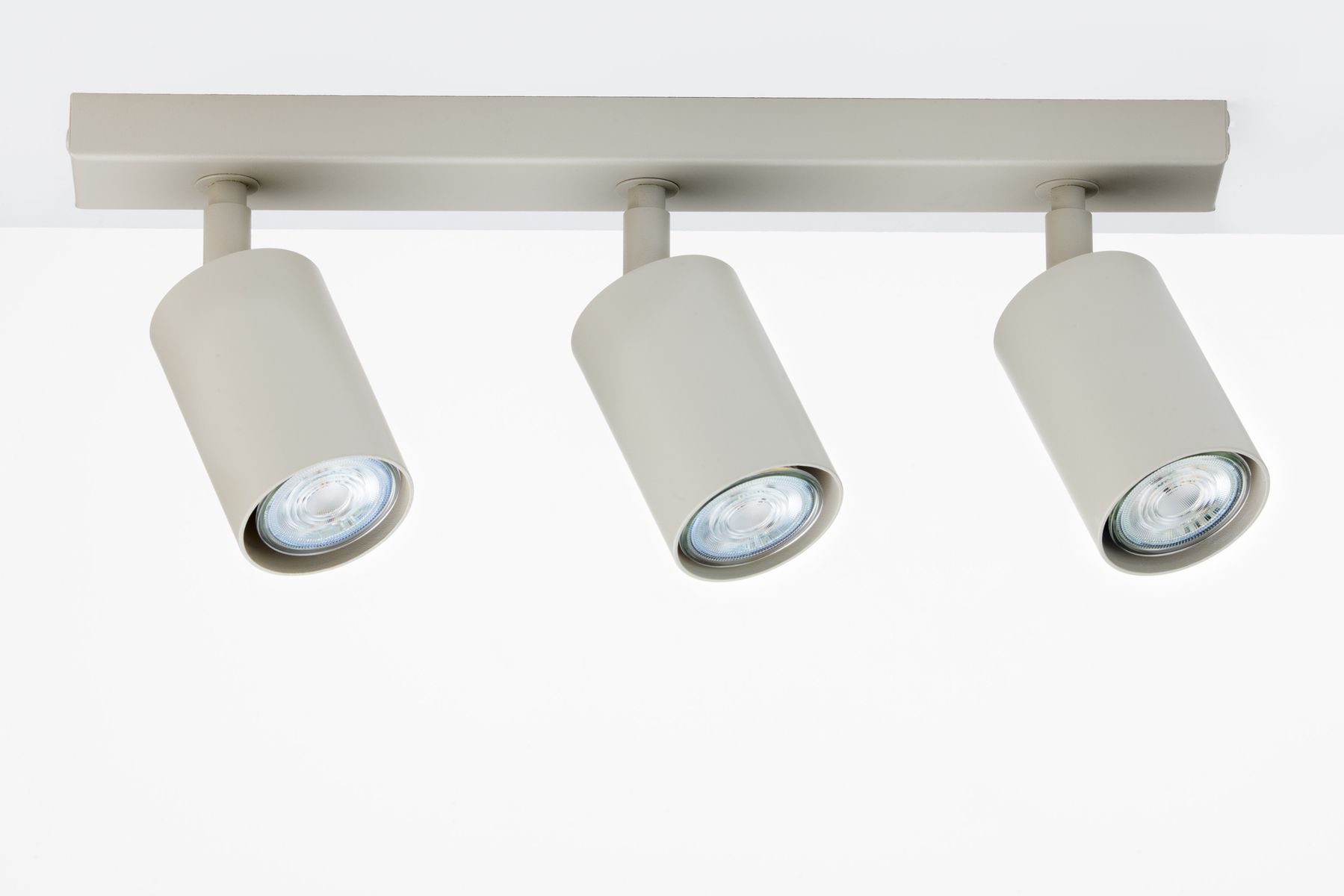Lampa sufitowa Zoom w kolorze szarym beżowym z trzema ruchomymi punktami świetlnymi GU10. Ujęcie frontalne, produkt zamontowany na prostokątnej podstawie, z widocznymi oprawkami reflektorów o okrągłej średnicy. Tło białe.