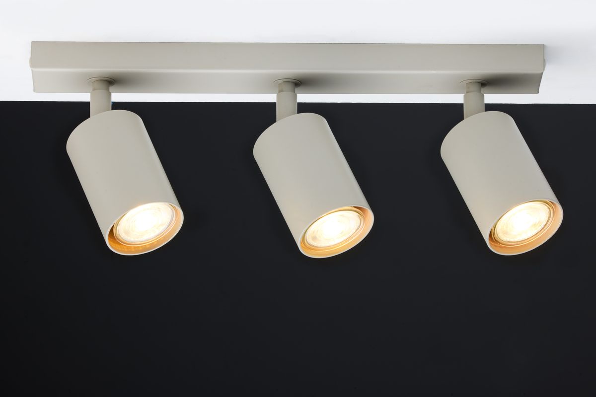 Lampa sufitowa Zoom w kolorze szaro-beżowym, z trzema ruchomymi reflektorami na prostokątnej podstawie. Reflektory mają cylindryczny kształt z widocznym źródłem światła, zamontowane na białym tle.