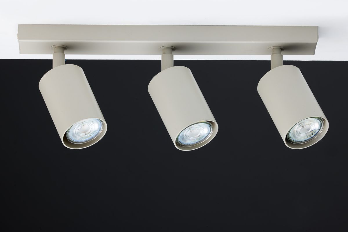 Lampa sufitowa Zoom w kolorze szarym beżowym z trzema punktami świetlnymi GU10. Ujęcie frontalne, mocowana do sufitu, z cylindrycznymi kloszami skierowanymi w dół, na jednolitym czarnym tle.