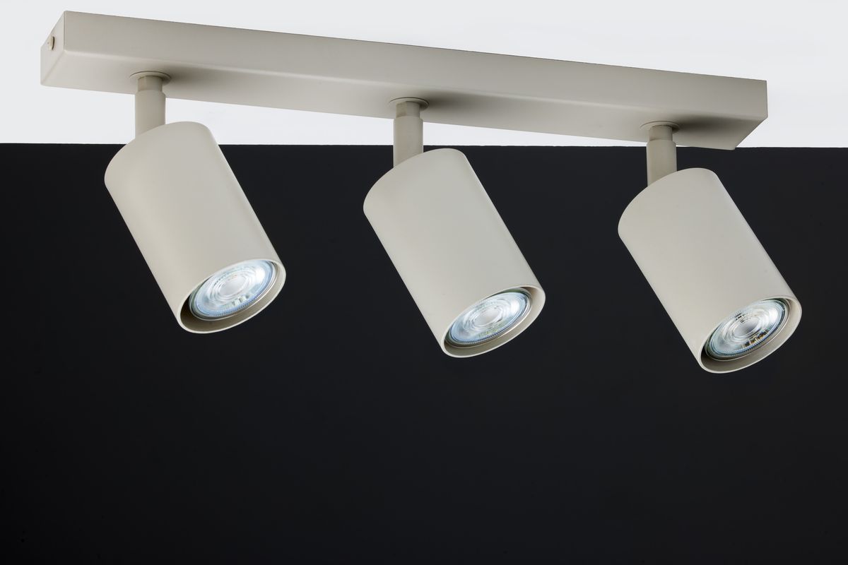 Lampa sufitowa Zoom w kolorze szarym beżowym, z trzema reflektorami GU10, zamontowana na prostokątnej podstawie. Reflektory mają cylindryczny kształt i są ustawione pod różnymi kątami. Tło ciemne, co podkreśla jasność lampy.