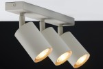 Szara beżowa lampa sufitowa (spot) z trzema oprawami GU10, zamontowana na prostokątnej podstawie. Reflektory o cylindrycznym kształcie, skierowane w różne strony, z widocznymi żarówkami. Tło ciemne, podkreślające design lampy.